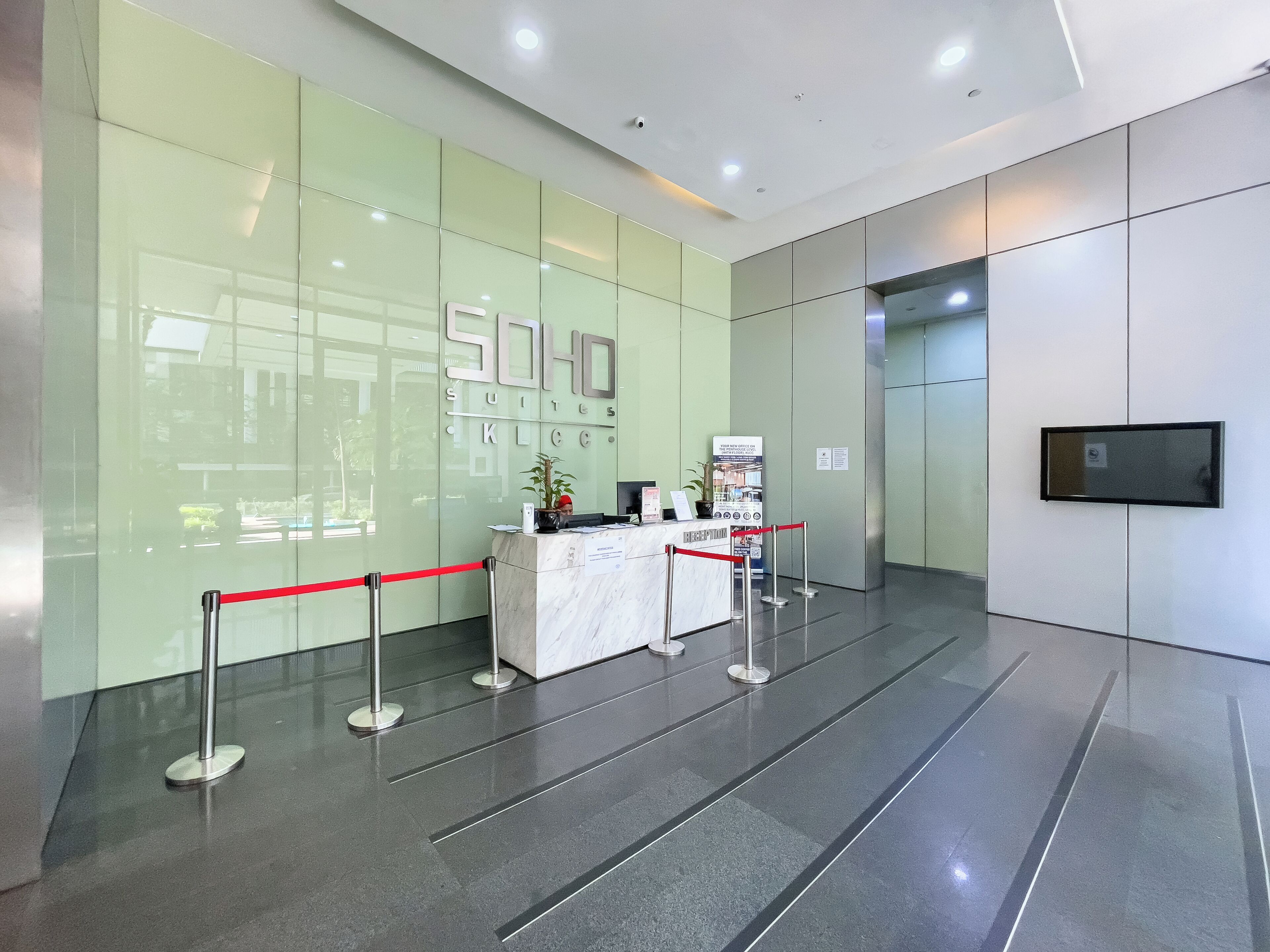 A hotel reception area with a glass wall, a reception desk, and a red barrier.