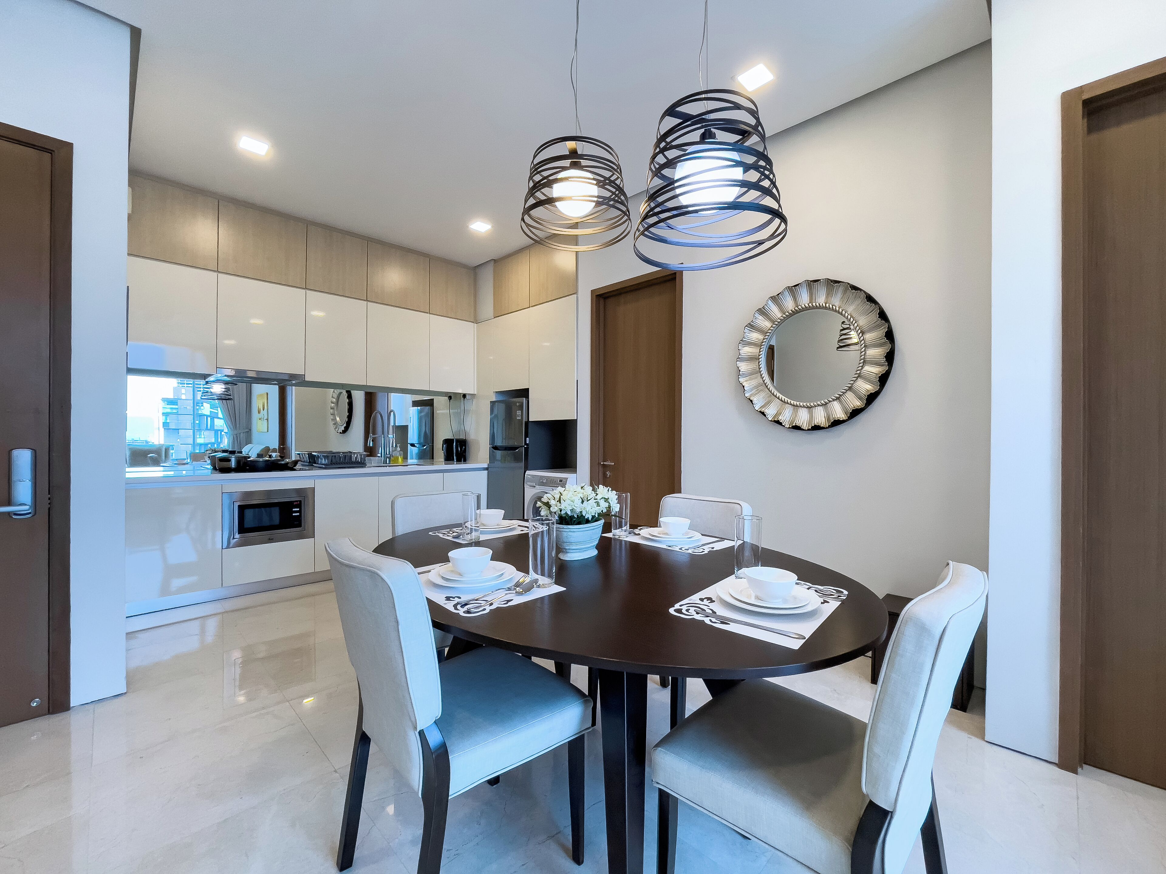 Un comedor moderno con una mesa redonda, cuatro sillas y un espejo decorativo en la pared.