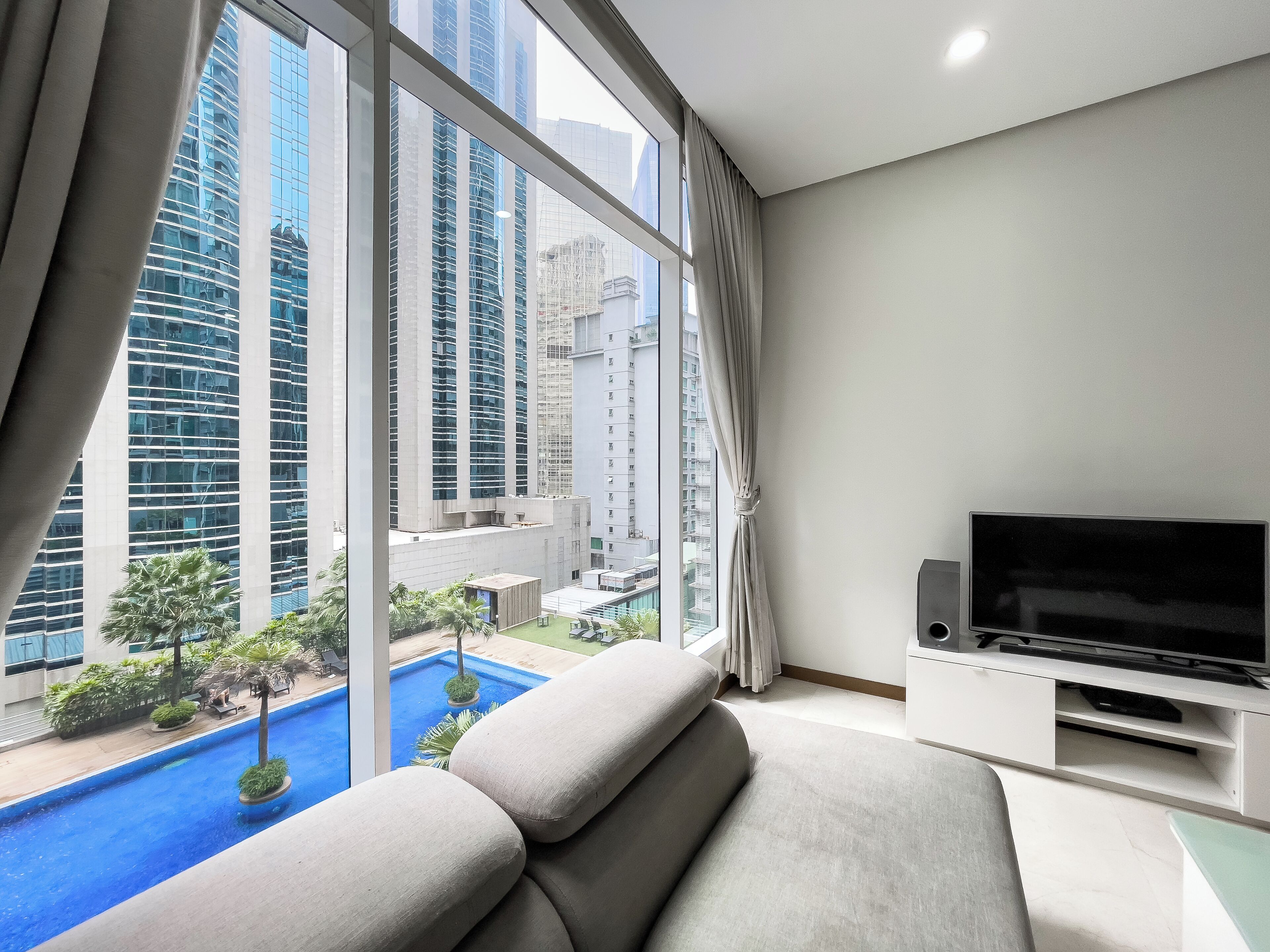 A modern living room with a large window, a flat-screen TV, and a pool view.