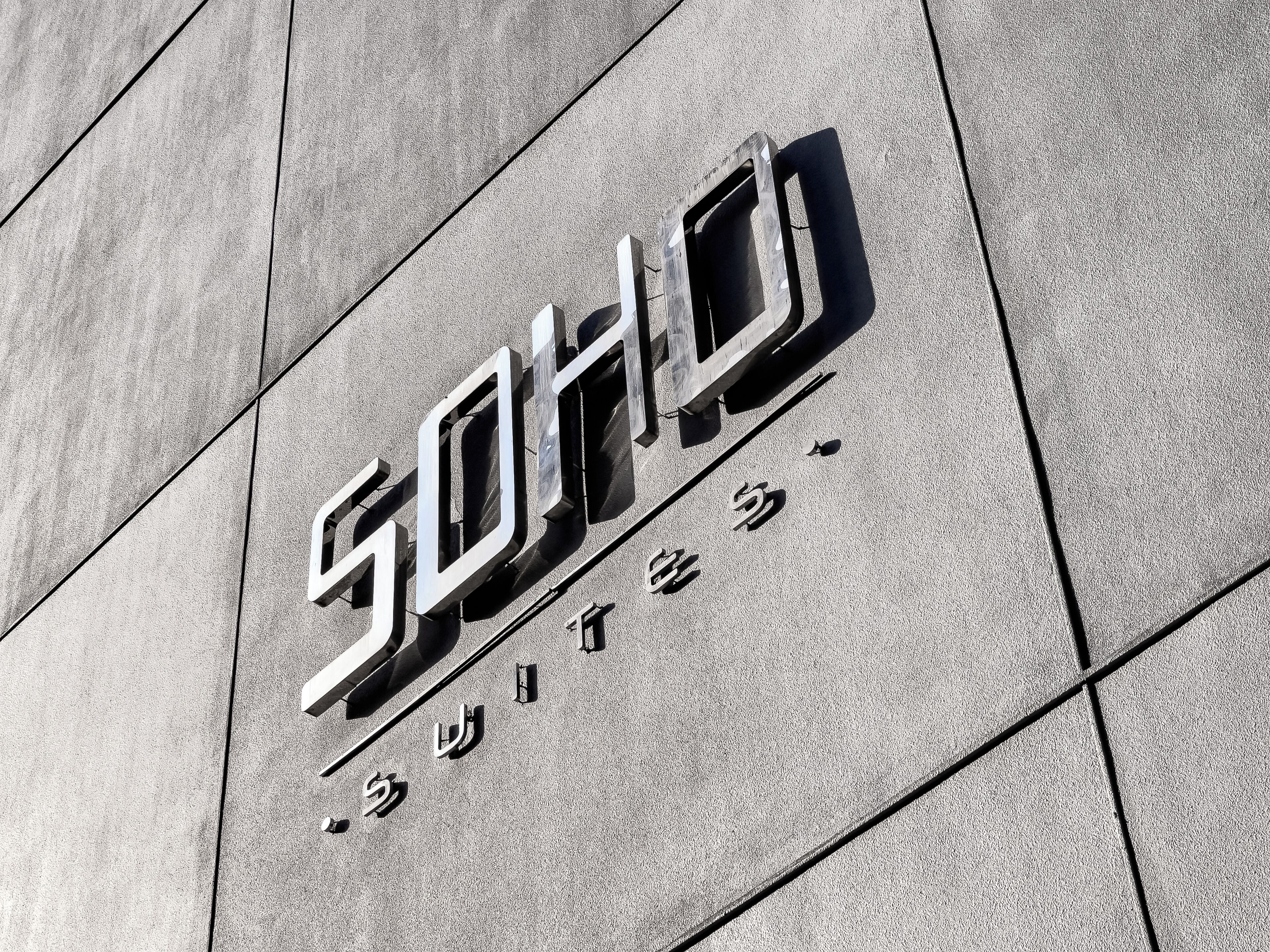 Un edificio con un moderno cartello geometrico che riporta le scritte 'SOHO' e 'SUITES'.