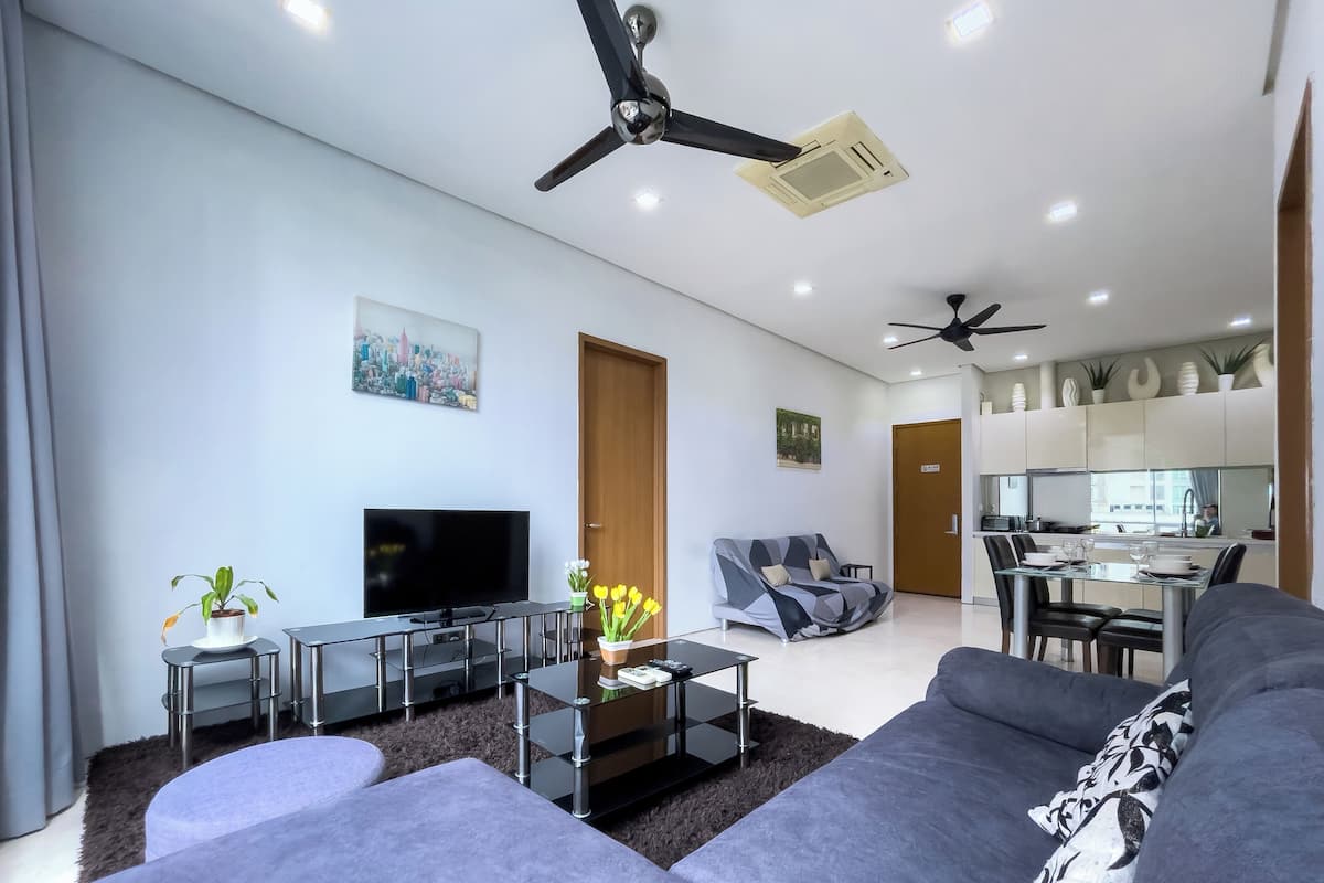 Un salon moderne avec un téléviseur à écran plat, des canapés gris, une table basse et un ventilateur de plafond.