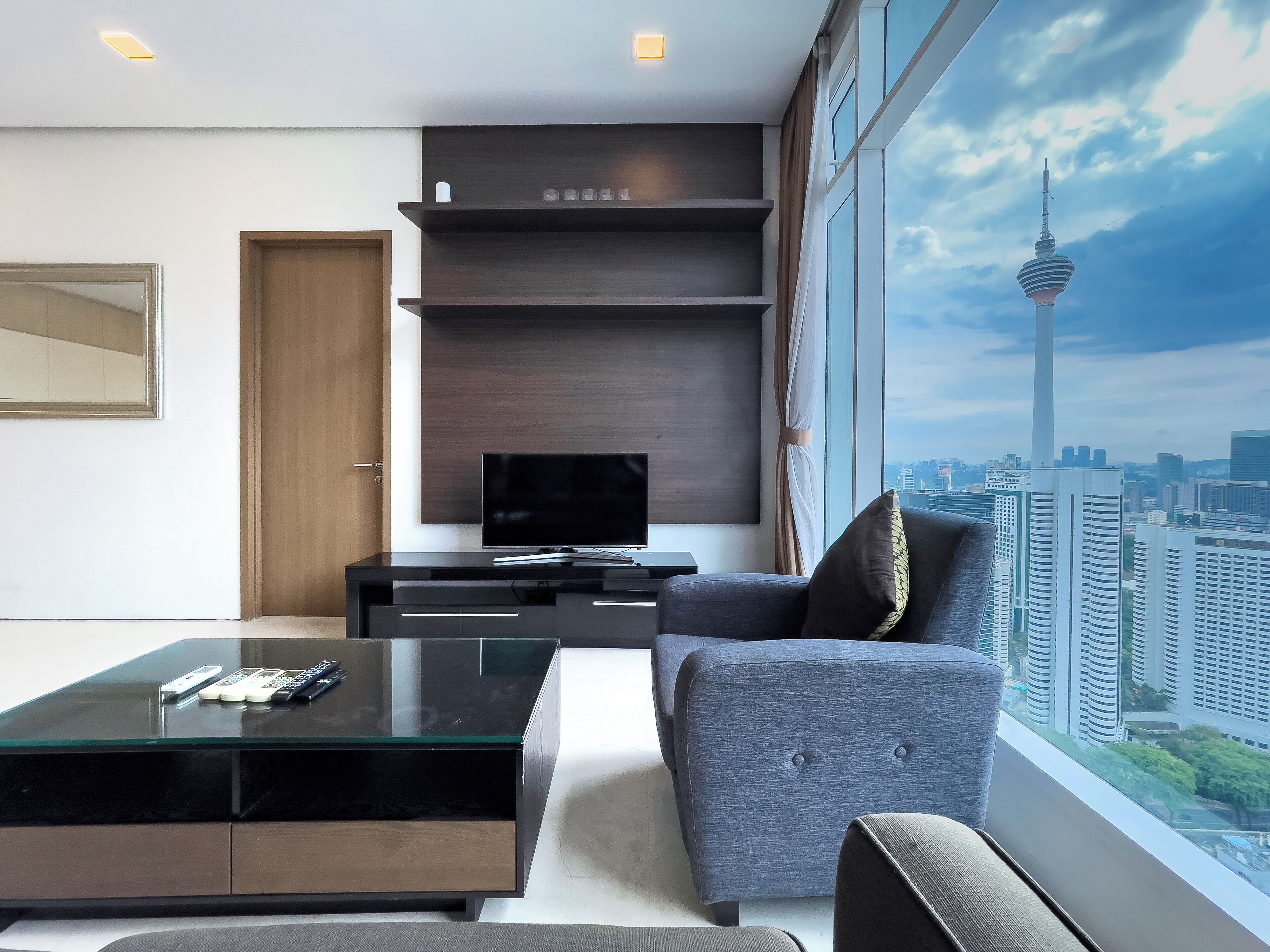 Una sala de estar moderna con un ventanal grande, un televisor de pantalla plana, una mesa de centro de vidrio y un sofá confortable.