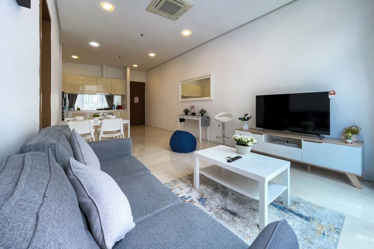 Un salon moderne avec un canapé gris, une table basse blanche et un téléviseur à écran plat posé sur un meuble en bois.