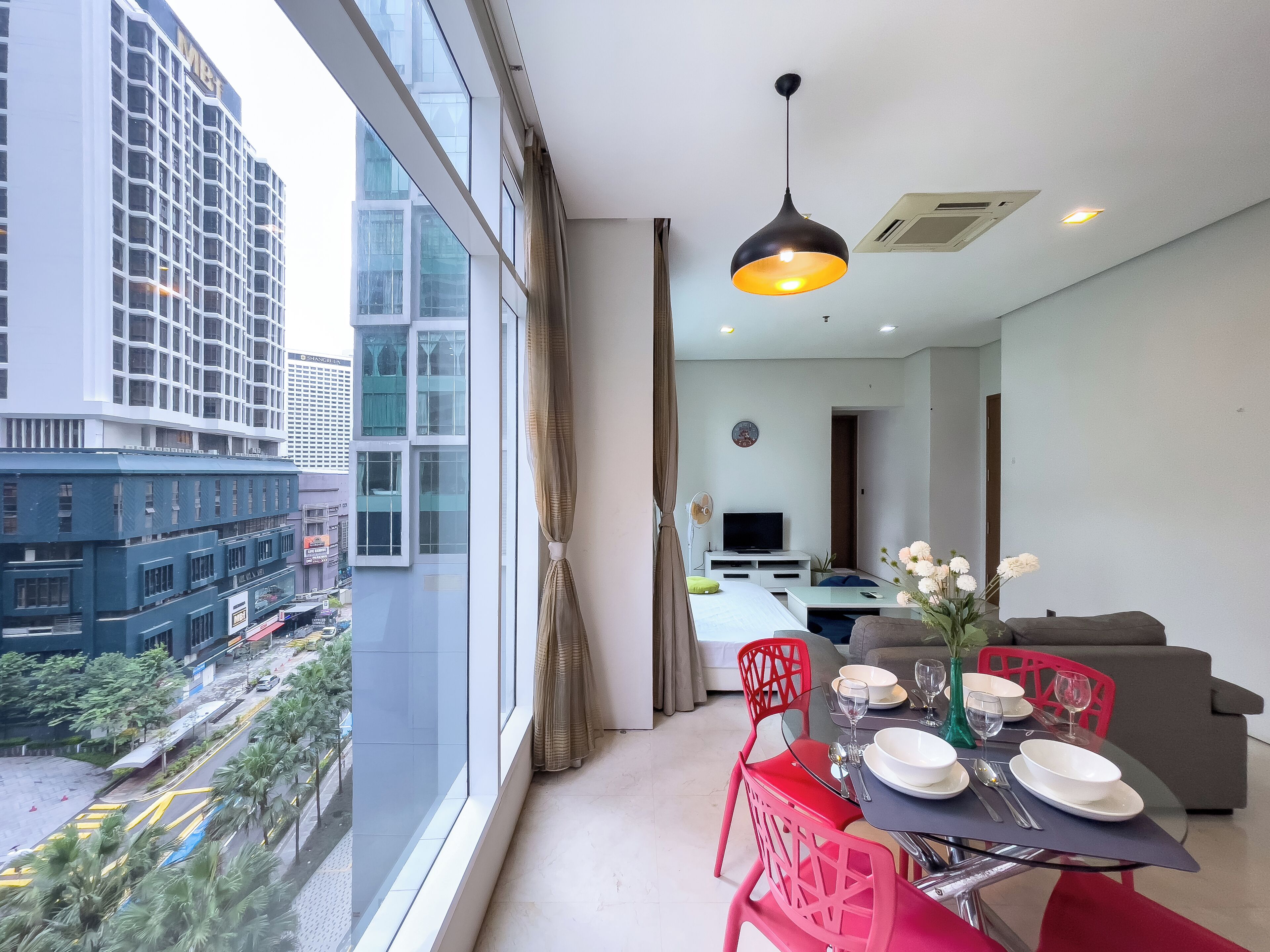 A modern hotel room with a dining area, large windows, and a view of the cityscape.