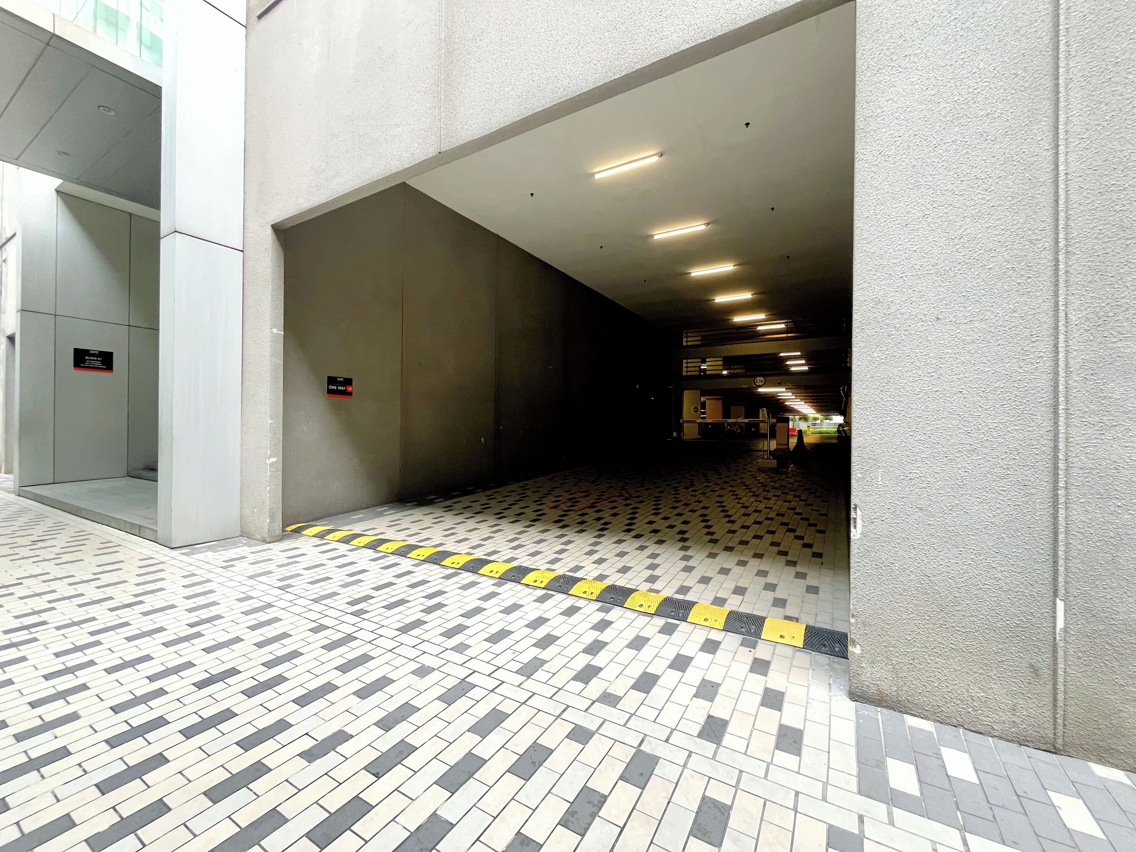 A tiled corridor with a checkered pattern, a one-way sign, and a door to a room.