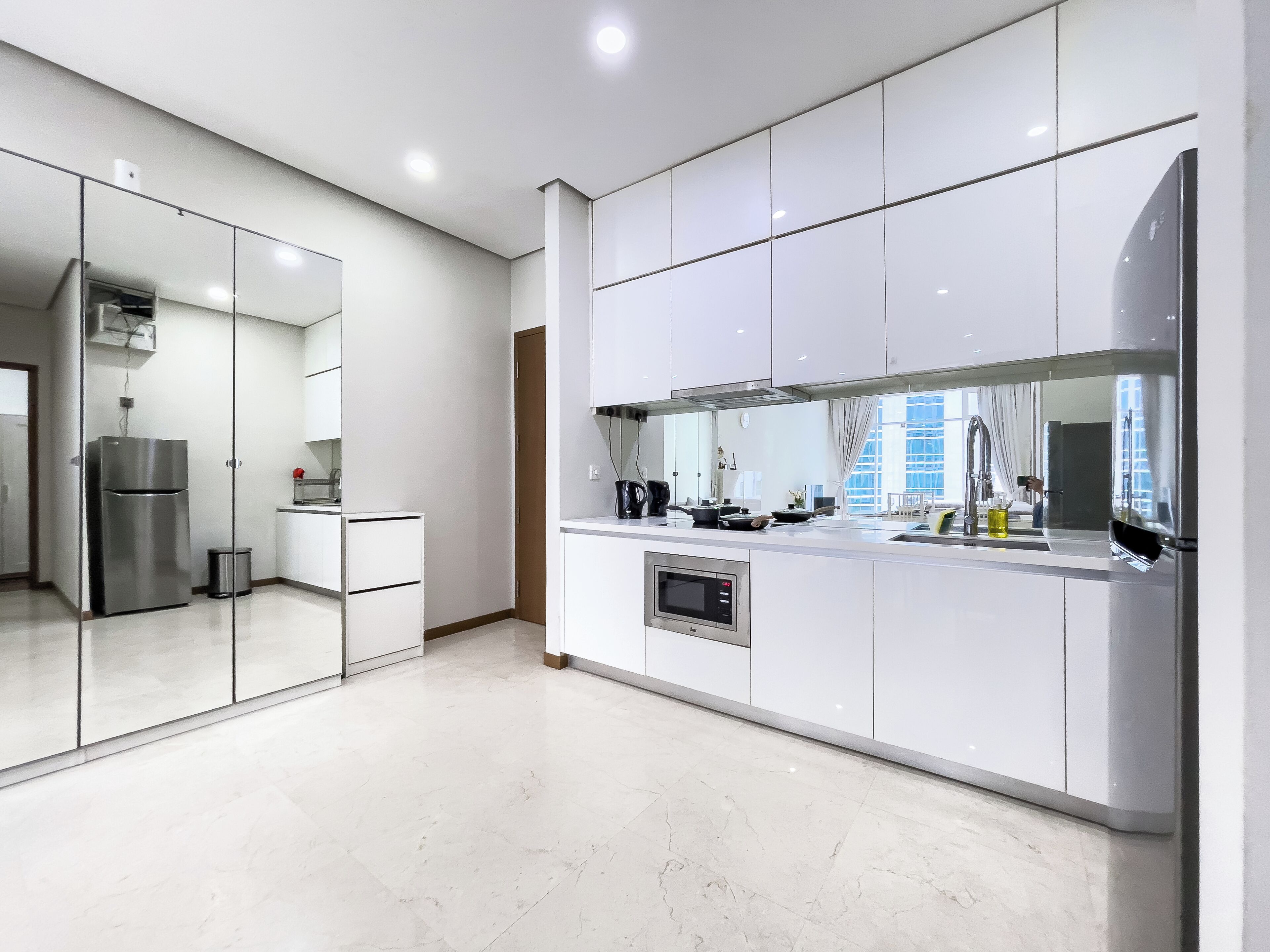 A modern kitchen with white cabinets, a stainless steel refrigerator, and a large window providing natural light.