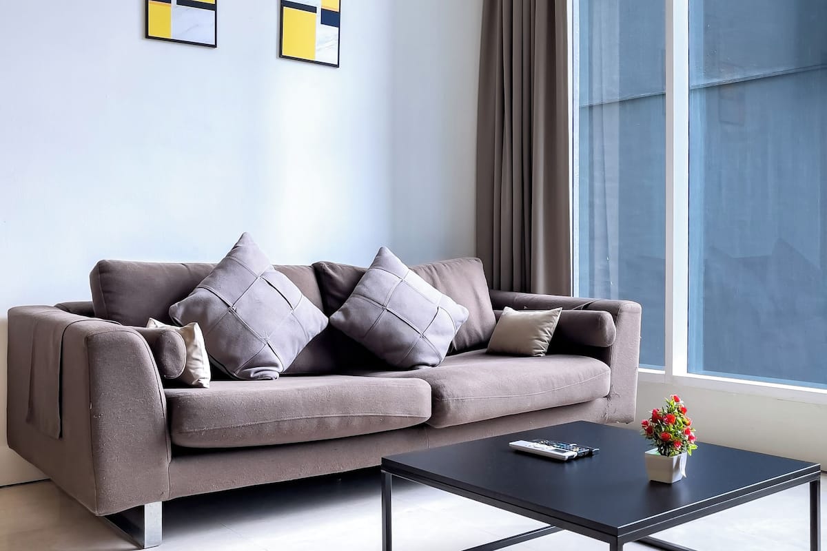 Un salon moderne avec un canapé gris, une table basse noire et des œuvres d’art abstraites accrochées au mur.