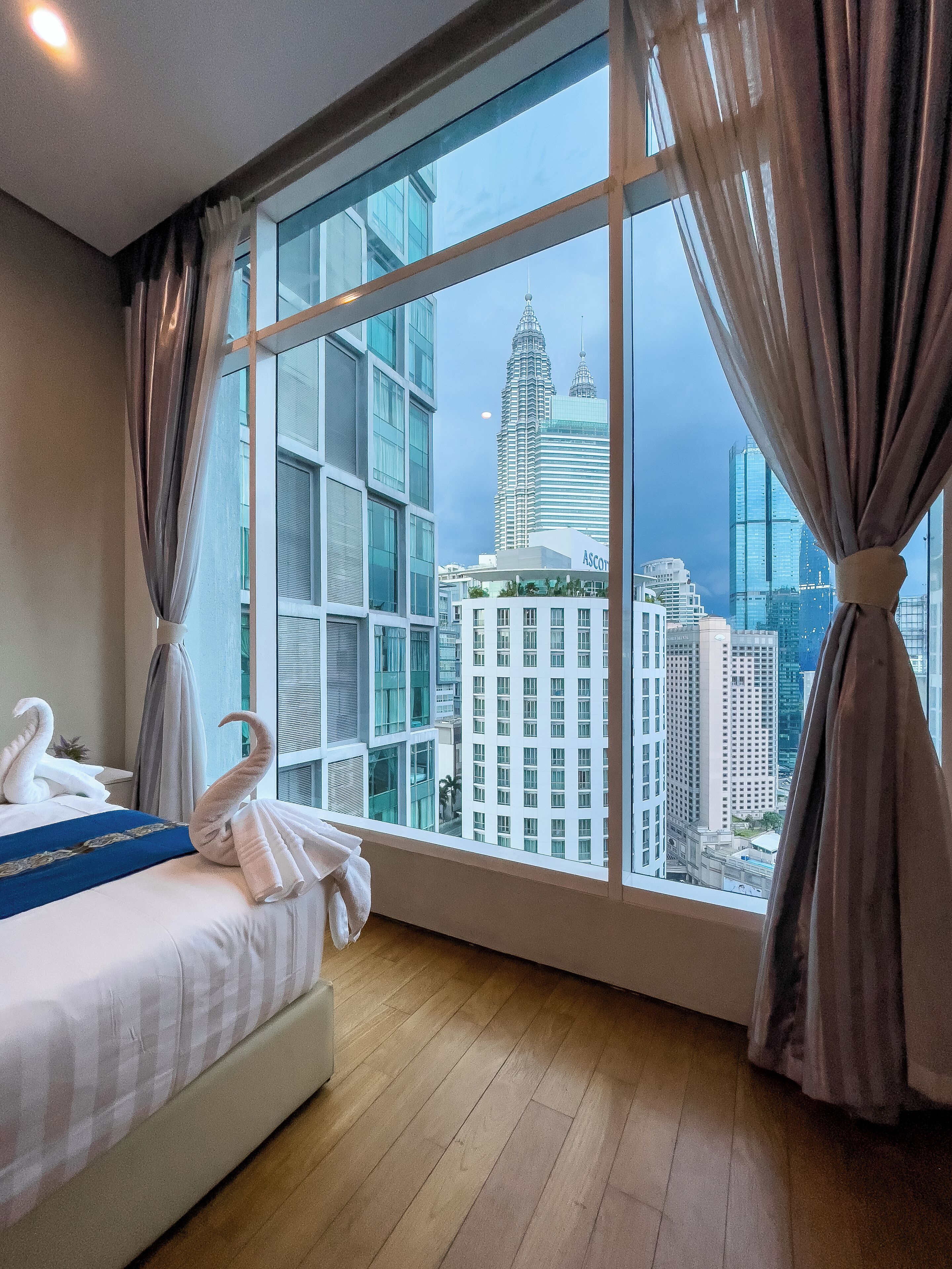 Habitación de hotel con un amplio ventanal que ofrece vistas del horizonte urbano, incluyendo un rascacielos destacado.