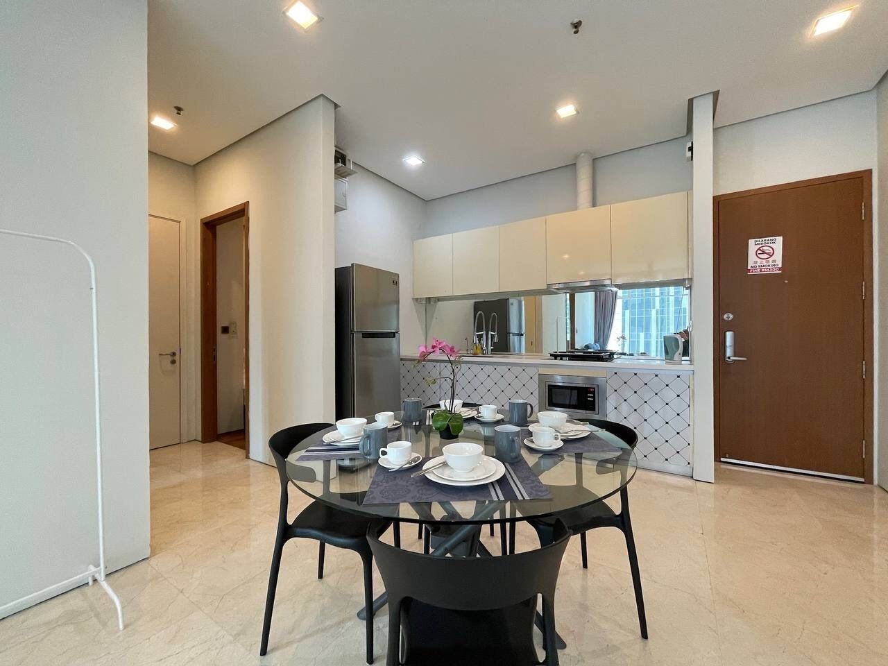 A modern kitchen with white cabinets, a dining table set for four, and a refrigerator.