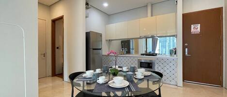 A modern kitchen with white cabinets, a dining table set for four, and a refrigerator.