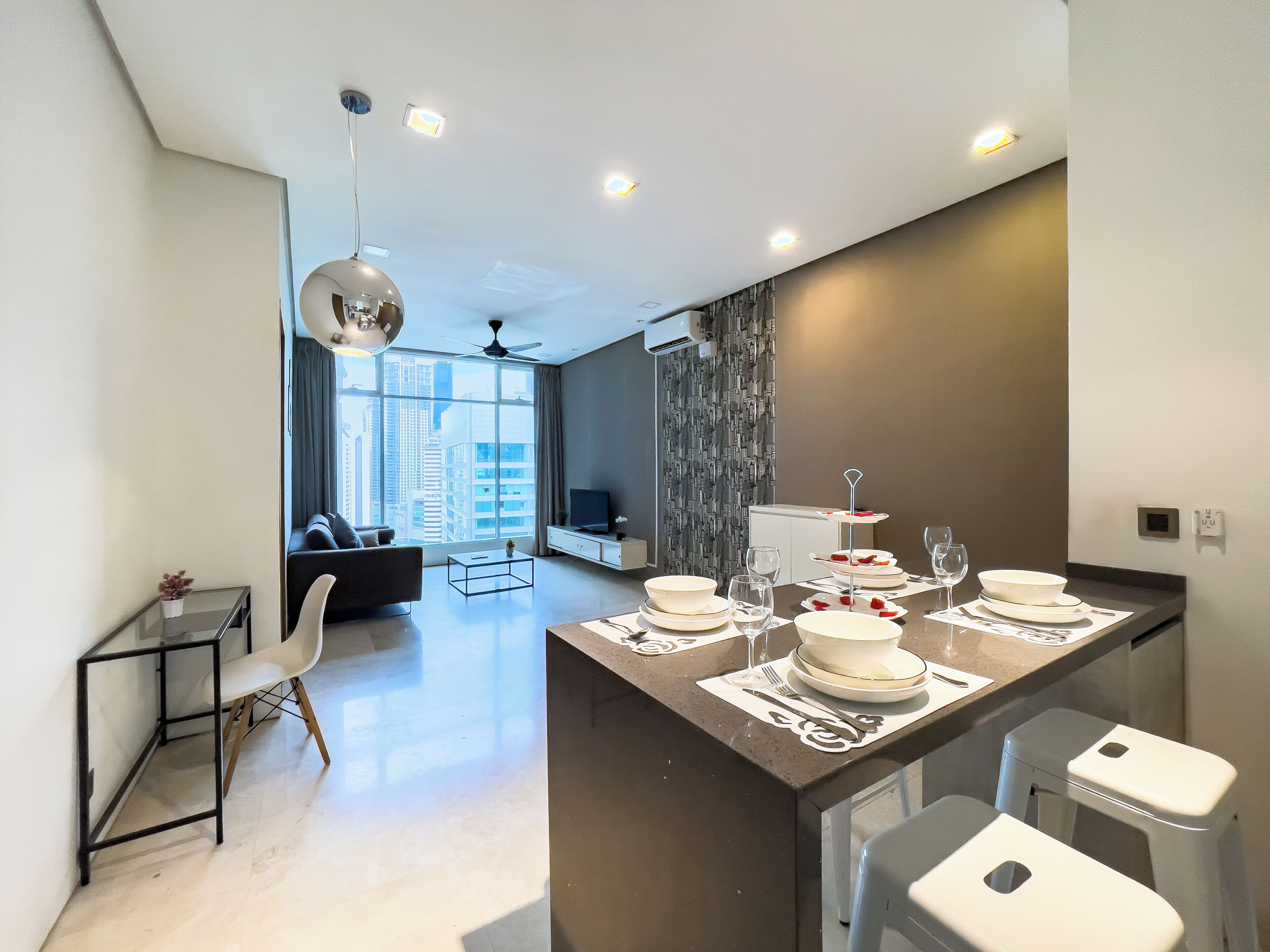 Cocina moderna con una isla central, mesa de comedor dispuesta con platos y vasos, y un rincón de estar con sofá y mesa de centro.