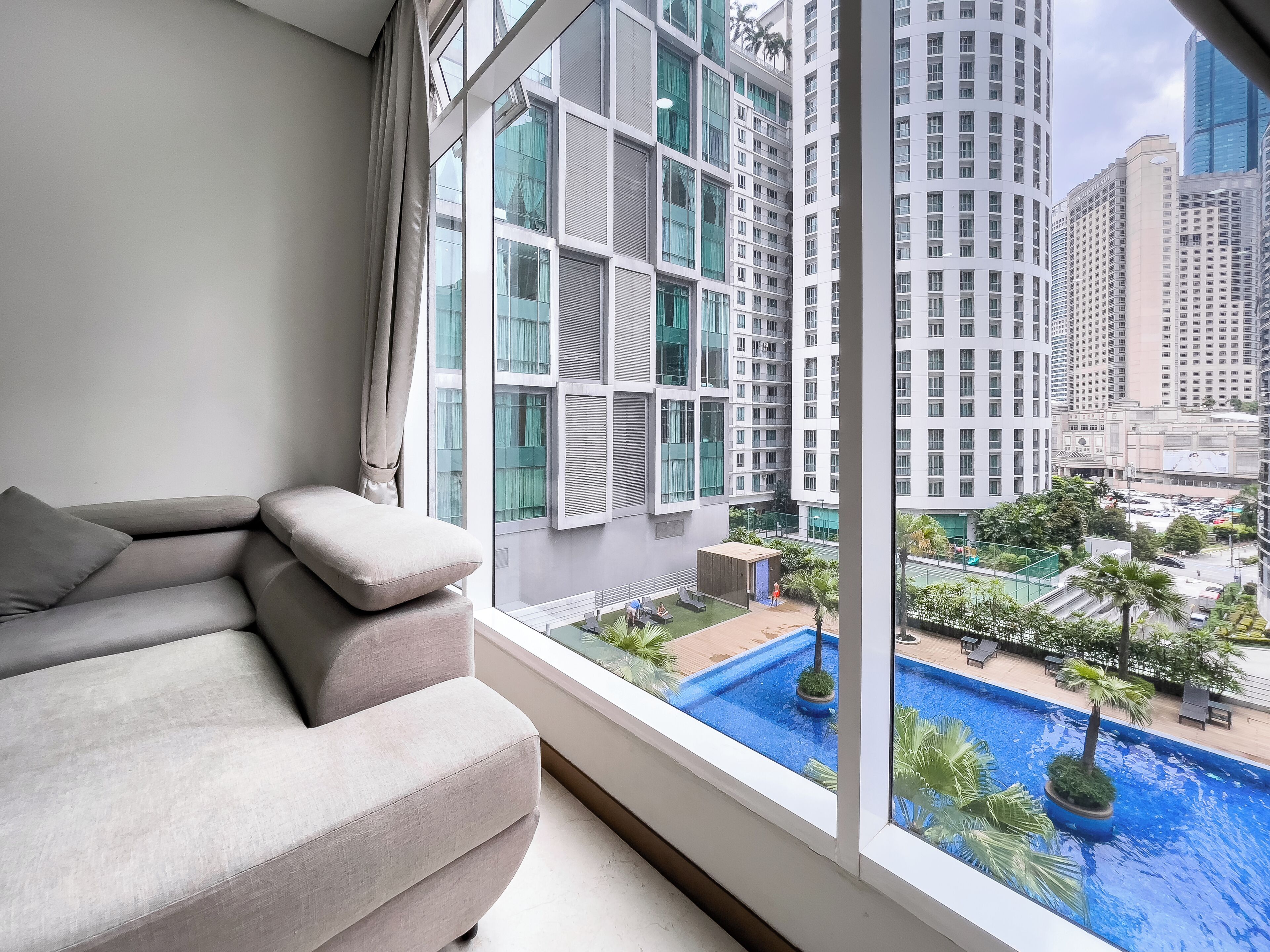 A modern living room with a large window overlooking a cityscape and a swimming pool.