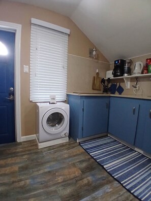 A laundry area with a washing machine, a blue cabinet, a coffee maker, and a striped rug.