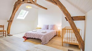 A bedroom with a sloped ceiling, a bed with floral bedding, a wooden crib, and a skylight. - Le Petit Chambi - CHAMBILLY (CHAMBILLY)