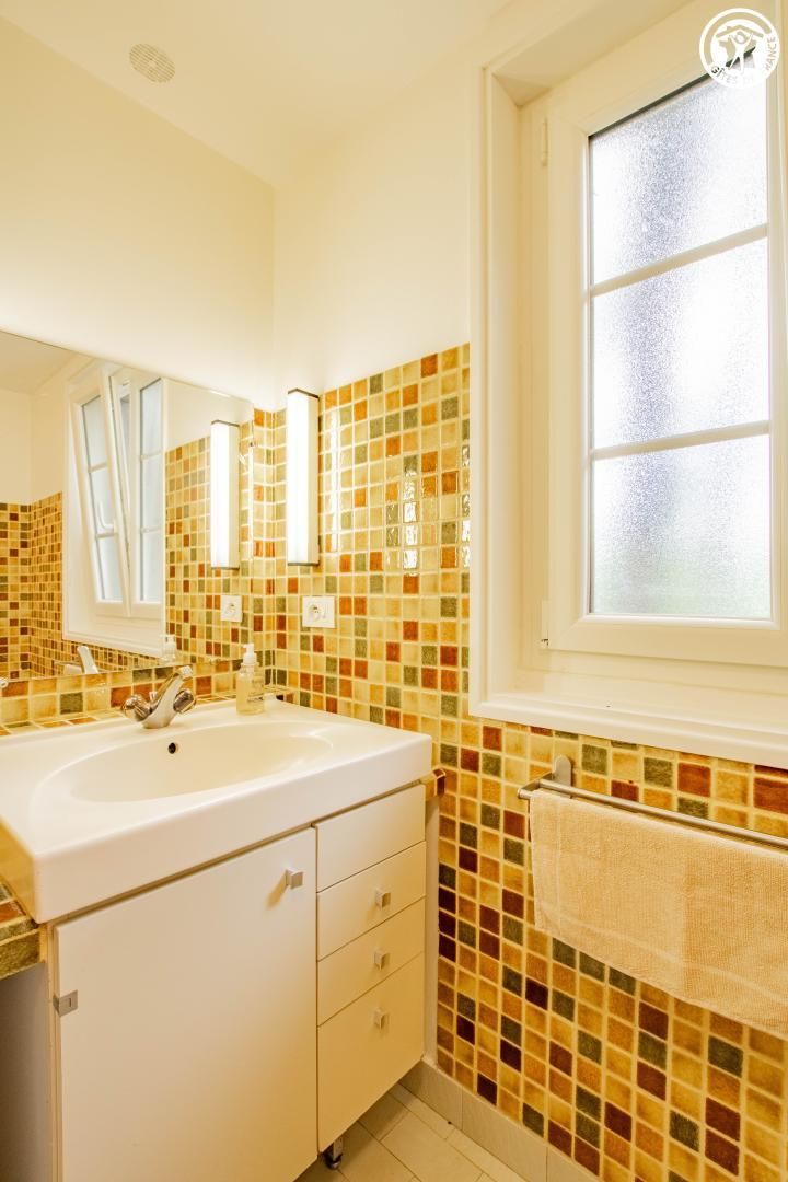 A bathroom with a large white sink, a mirror, and a window with frosted glass.