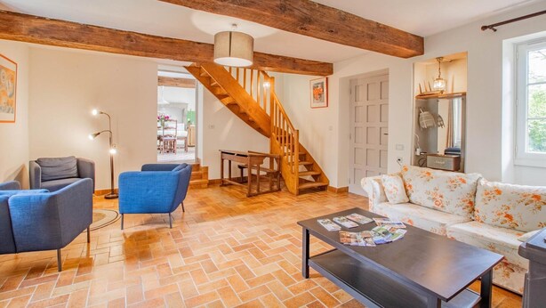 A spacious living room with a herringbone floor pattern, a wooden staircase, a sofa with floral upholstery, and a coffee table with magazines. - Le Petit Chambi - CHAMBILLY (CHAMBILLY)