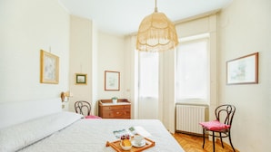 A neatly arranged bedroom with a large bed, a wooden dresser, a chair, and a window with curtains. - Imperatrice apartment by Wonderful Italy (Sanremo)