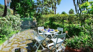 A garden patio with a stone pathway, white chairs, and a table set with plates, glasses, and a bottle. - Imperatrice apartment by Wonderful Italy (Sanremo)