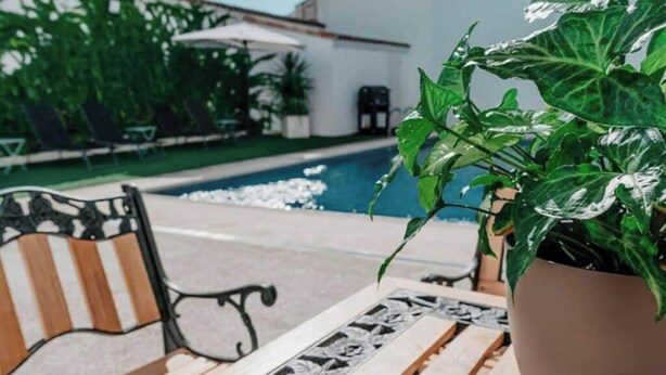 Un área junto a la piscina con un banco de madera, una planta en maceta y una mesa de azulejos.