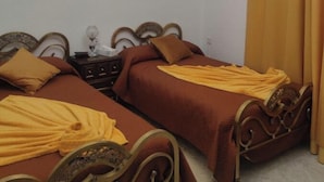 Una habitación con dos camas, cada una con una colcha marrón y una manta amarilla. Hay un cuadro en la pared y una cortina en la ventana.