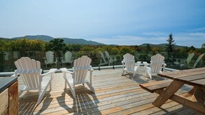Une terrasse en bois avec des fauteuils Adirondack et une table de pique-nique, offrant une vue sur un paysage montagneux.