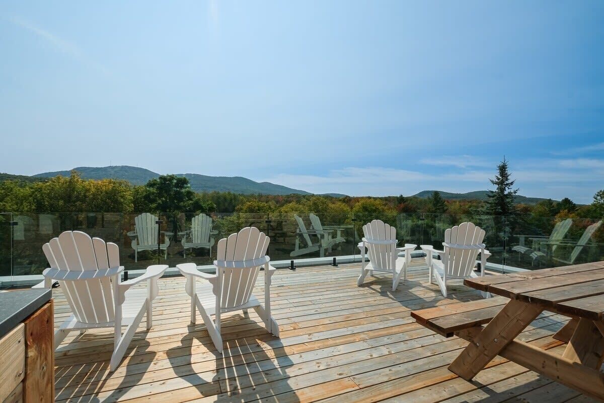 Terraza de madera con sillas Adirondack y una mesa de picnic, con vistas a un paisaje montañoso.