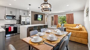 A modern kitchen with a dining area, a sofa, and a TV.