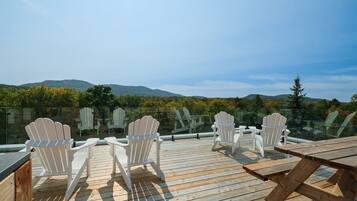 A wooden deck with Adirondack chairs and a picnic table, overlooking a mountainous landscape.