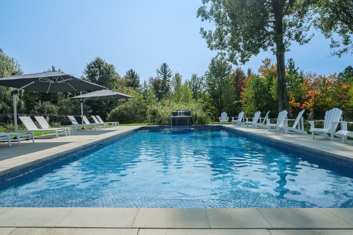 A swimming pool with a waterfall feature, surrounded by white lounge chairs and umbrellas.