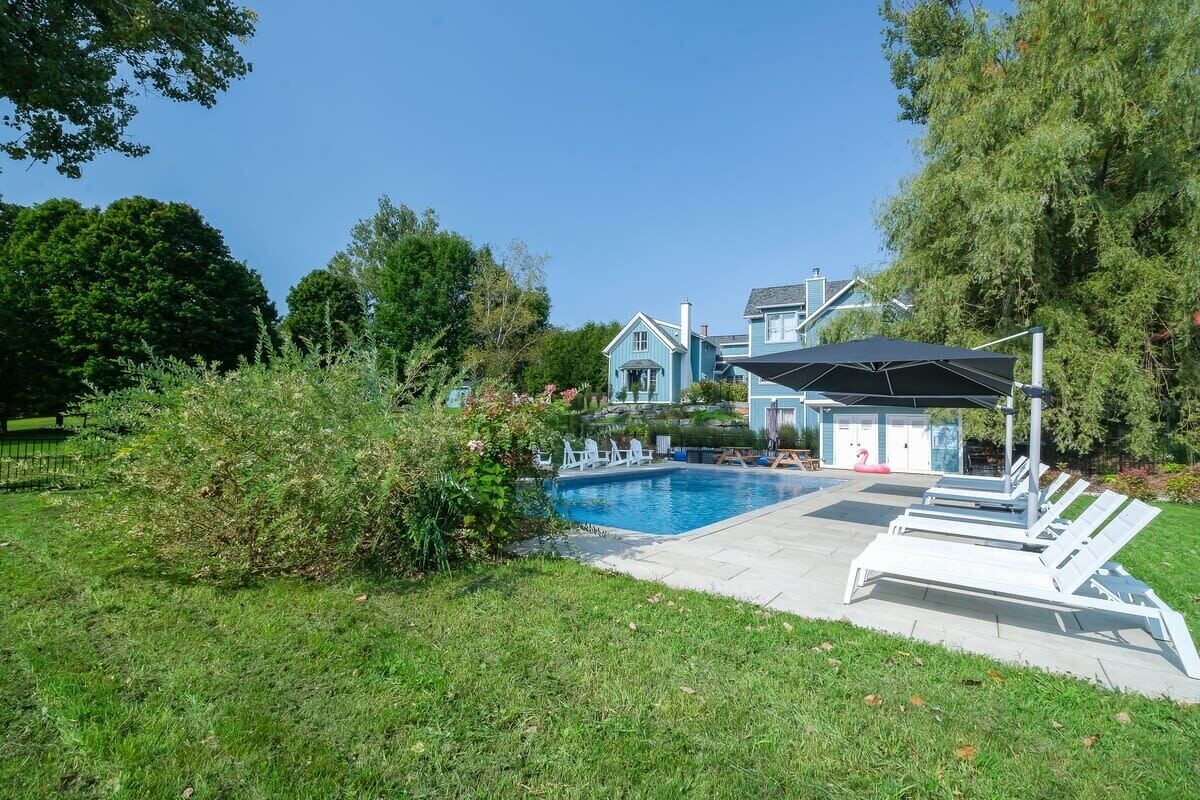 A swimming pool with lounge chairs, a covered area, and a house in the background.