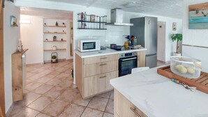 Cocina compacta con microondas, horno y lavabo. Cuenta con armarios de madera y encimera blanca.