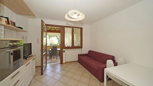 A compact living space with a kitchenette, a red sofa, a dining table, and a window with curtains.