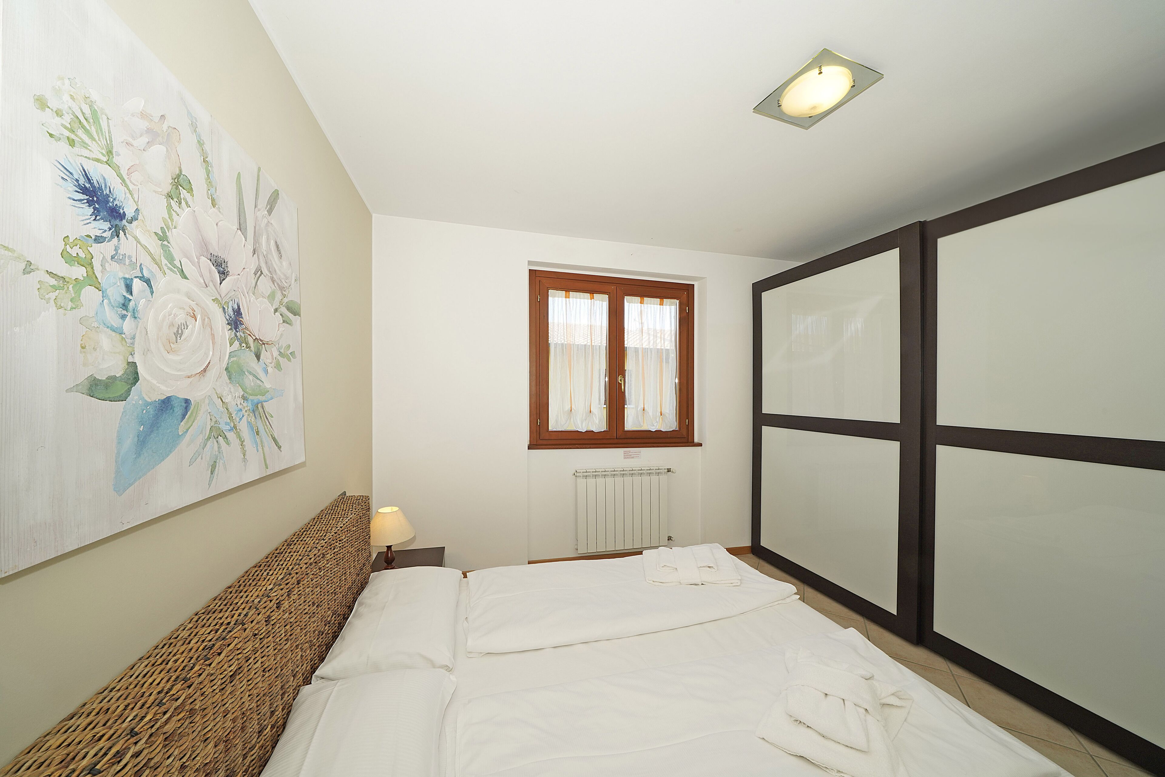 A bedroom with a bed, a painting on the wall, a window with curtains, and a radiator.