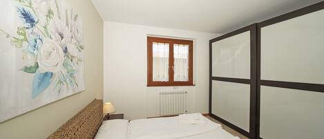 A bedroom with a bed, a painting on the wall, a window with curtains, and a radiator.