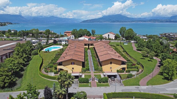 A residential area with two yellow houses, a swimming pool, and a view of the sea and mountains.