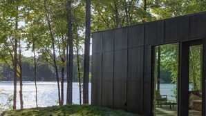 Un edificio moderno con una porta vetrata che si apre su una zona salotto esterna, affacciata su un lago.