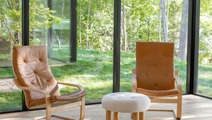 Una camera moderna con ampie finestre, due poltrone in pelle, un poggiapiedi in legno e un soffitto in vetro.
