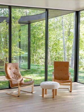 A modern room with large windows, two leather chairs, a wooden ottoman, and a glass ceiling.