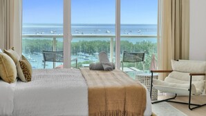 Une chambre avec une grande fenêtre, un lit, une chaise et une vue sur la mer et les bateaux.