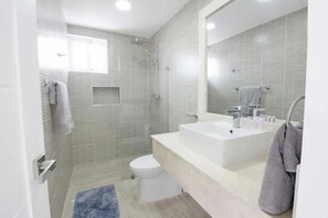 A modern bathroom with a shower, toilet, and a large sink with a mirror.