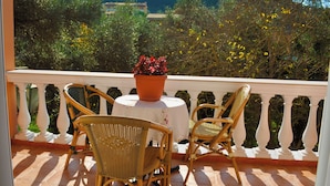 Ein Balkon mit Korbstühlen und einem Tisch, mit Blick auf einen Garten mit Bäumen und einem Berg im Hintergrund.