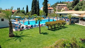 Ein Poolbereich mit Liegestühlen und Sonnenschirmen, umgeben von Grünflächen und Gebäuden.