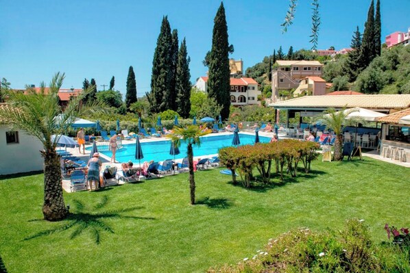 A pool area with lounge chairs and umbrellas, surrounded by greenery and buildings.