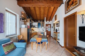 A compact kitchen with wooden beams, a dining table with chairs, a sofa, and a television. - Poggio sul Clisi 30 Apartment by Wonderful Italy (Villanuova sul Clisi)