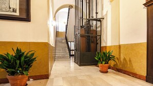 A hallway with marble flooring, two potted plants, a staircase, and a metal gate. - Studio nel Cuore della Citta' by Wonderful Italy (Bologna)