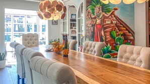 Comedor con una larga mesa de madera, sillas acolchadas y un mural de una persona sosteniendo un cactus.