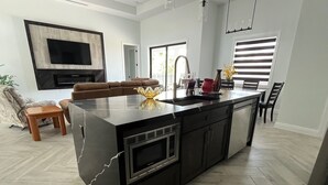 A modern kitchen with a large island, built-in oven, and a flat-screen TV mounted on the wall. - Sueños Villa (Cape Coral)