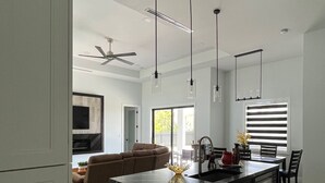 A modern kitchen with a central island, pendant lights, and a dining area with chairs and a table. - Sueños Villa (Cape Coral)