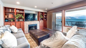 A modern living room with a fireplace, a large flat-screen TV, and a view of the sea. - GrandView 303 -2 Bedroom Waterfront condo (Chelan)