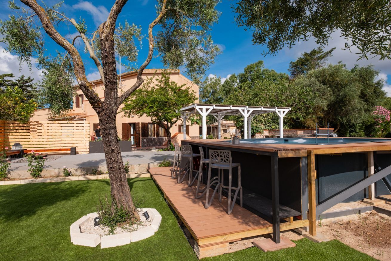 Una terraza de madera con mobiliario exterior, un pérgola y un edificio al fondo.